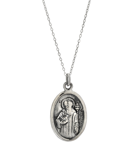 The Sterling Silver Saint Benedict Protect Us Pendant Necklace, 18", features an elegant oval design with a raised image of the saint and inscriptions, hanging from a delicate chain.